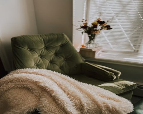 A comfortable chair with a blanket near a window